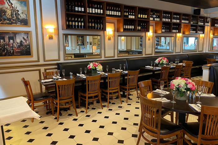 Restaurant interior with tables set for dining, wine racks, and floral centerpieces.