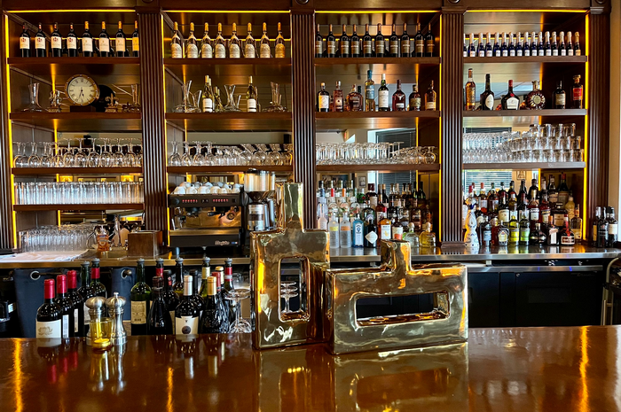 Bar with liquor bottles on shelves and decorative brass sculptures on the wooden counter.