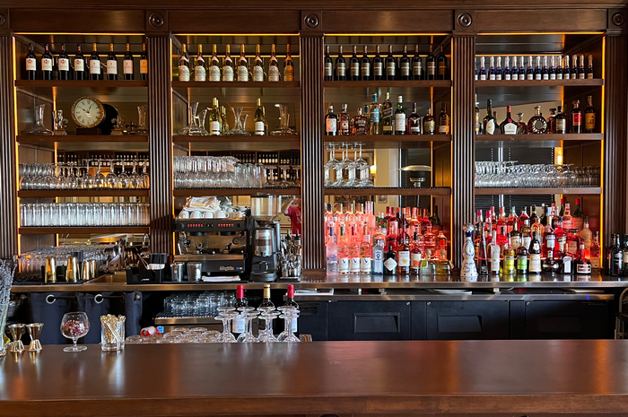 Bar with wooden counter, lit bottles and glassware on shelves.