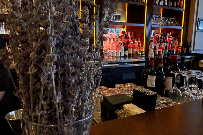 Dried lavender in a vase on a bar, with liquor bottles and glasses in the background.