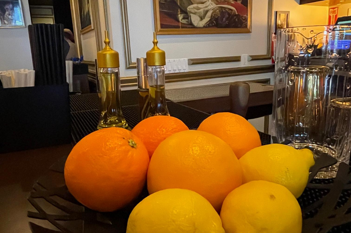 Oranges and lemons in a bowl, with oil bottles, and a glass of water, in a restaurant.