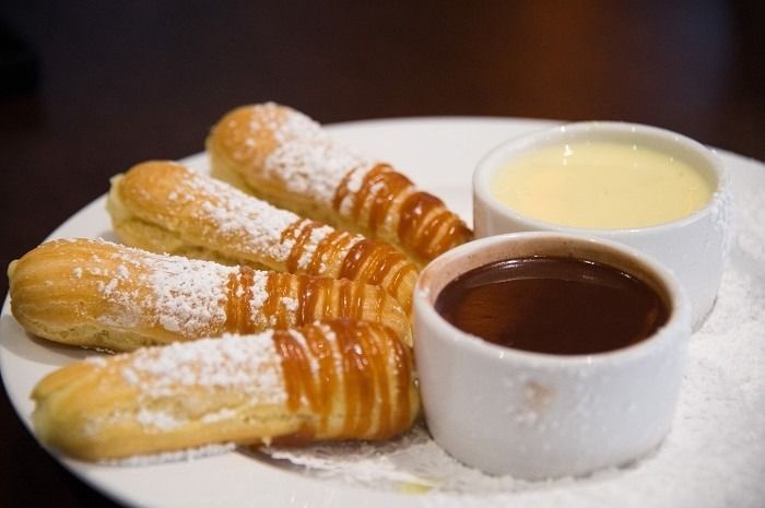 Eclairs dusted with powdered sugar and drizzled with caramel, served with chocolate and vanilla dipping sauces.