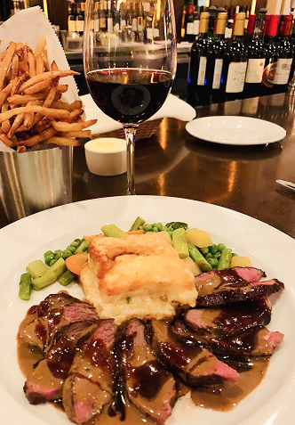 Plate of steak, potatoes, and vegetables with gravy, fries, and red wine in a restaurant.