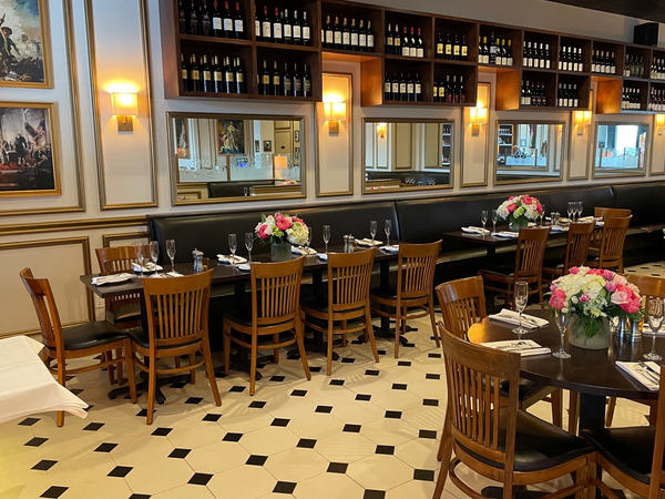 Restaurant interior with tables set for dining, shelves of wine, mirrors, and floral centerpieces.