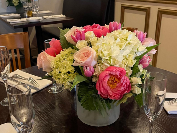 A floral centerpiece with pink and white flowers on a restaurant table set for dining.