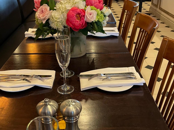 Formal dining table set with flowers, silverware, glasses.