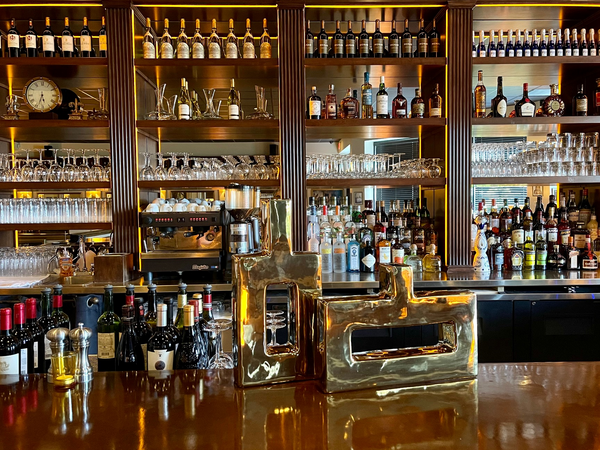 Bar with liquor bottles on shelves, espresso machine, and gold sculptures on a wooden counter.