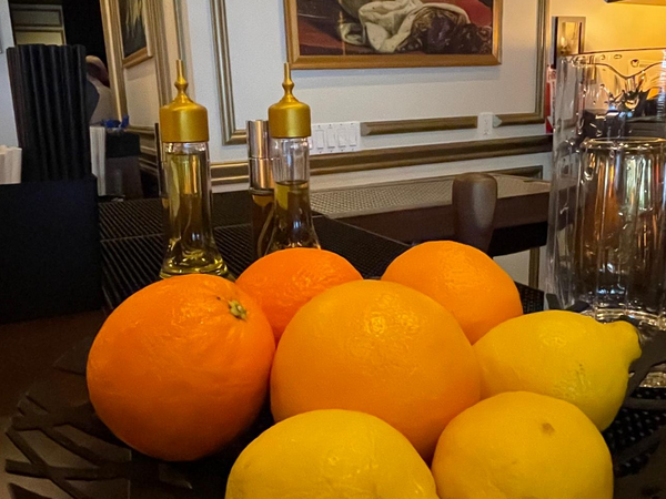 Oranges and lemons in a dark bowl, with oil bottles in the background.