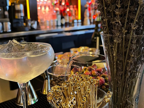Cocktail with ice, bar setting; dried lavender, rosebuds, and cocktail picks in focus.