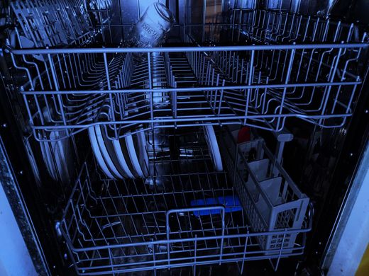 Blue-lit dishwasher rack filled with dishes and utensils inside a kitchen appliance