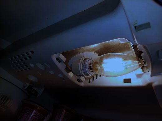 Close-up of a glowing light bulb inside a ceiling fixture, with dark surrounding panels.