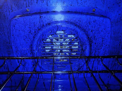 Blue-lit oven interior with a metal rack and fan at the back