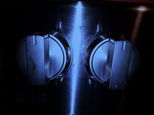 Close-up of two blue-lit metallic knobs on a dark appliance panel