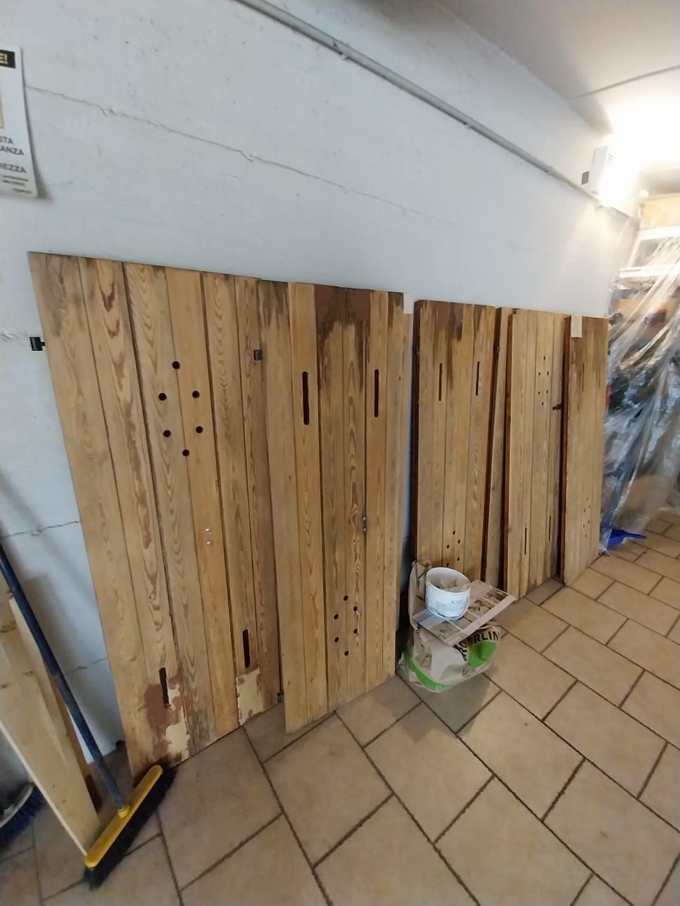 Due pannelli di legno usurati appoggiati a una parete bianca in una stanza con pavimento piastrellato.