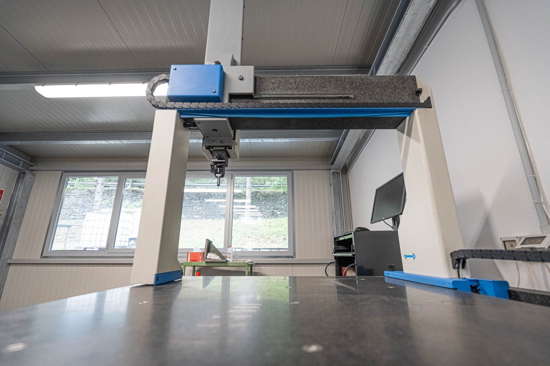 Grande stampante 3D industriale in un'officina luminosa con finestre e un tavolo da lavoro di fronte