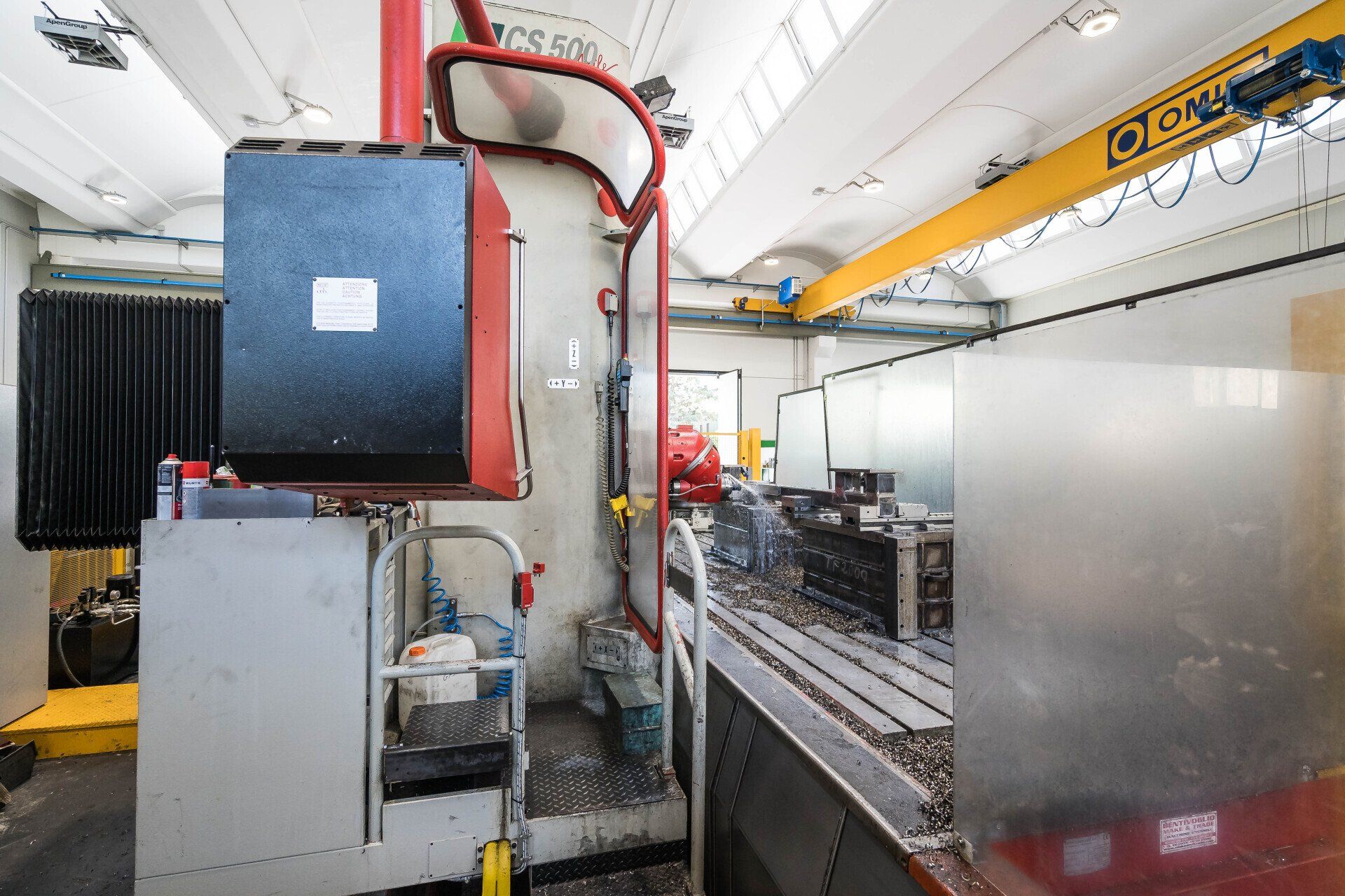 Macchinario industriale all'interno di una stanza di fabbrica pulita con nastro trasportatore metallico e tubature rosse.