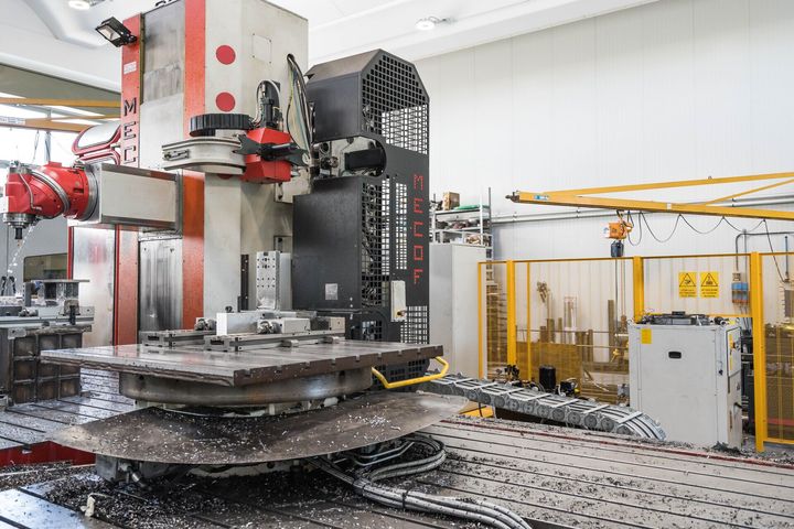 Grande macchinario industriale in una fabbrica, con piattaforma metallica e recinzione di sicurezza nelle vicinanze.
