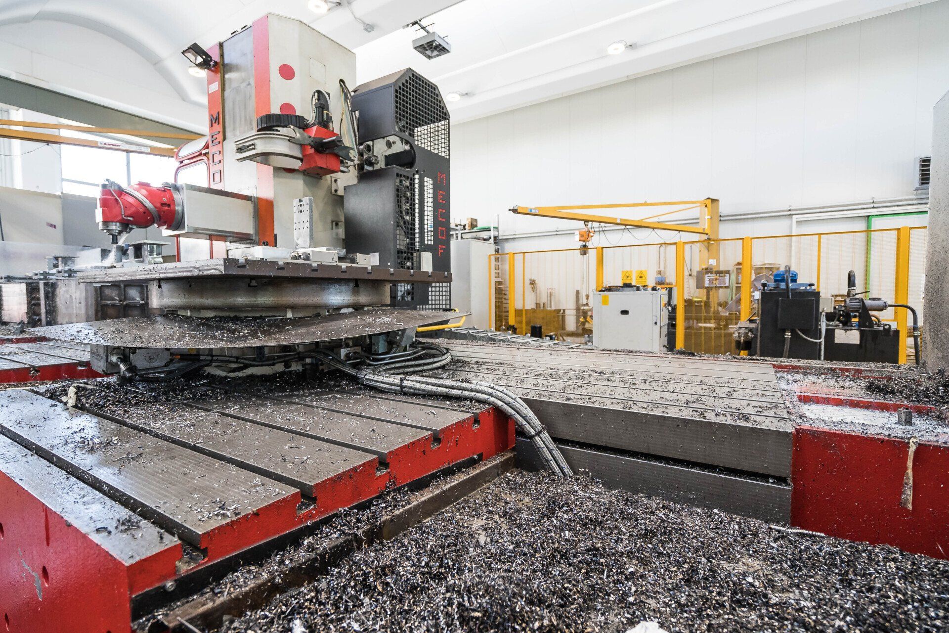 In un'officina, una grande macchina industriale taglia lastre di pietra, circondata da attrezzature e detriti di colore rosso e grigio.