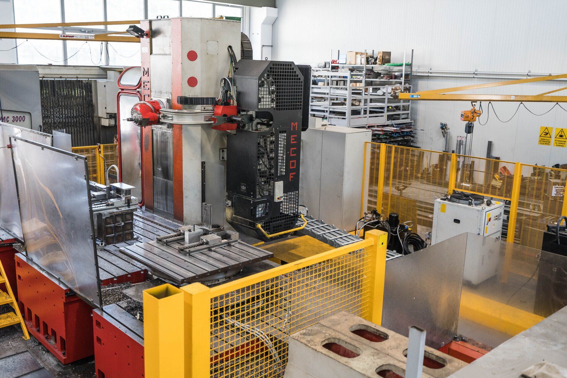Macchinario industriale in una fabbrica, con recinzione di sicurezza gialla e attrezzature metalliche sul pavimento.