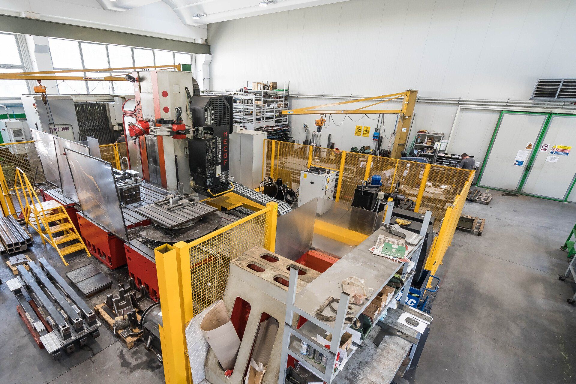 Officina industriale con macchinari gialli, componenti metallici e banchi da lavoro in un luminoso locale di fabbrica.