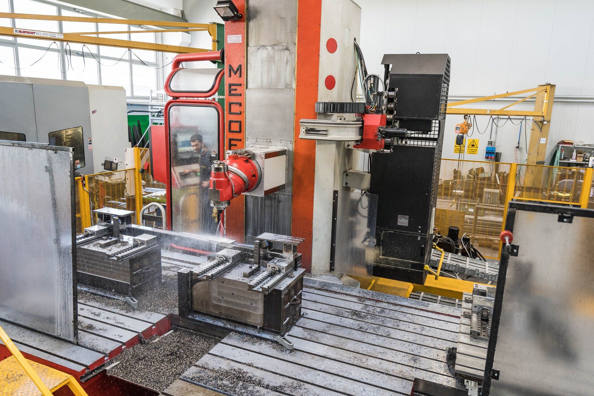 Macchinario industriale in una fabbrica, con componenti metallici su un banco di lavoro e tubature di sicurezza arancioni.