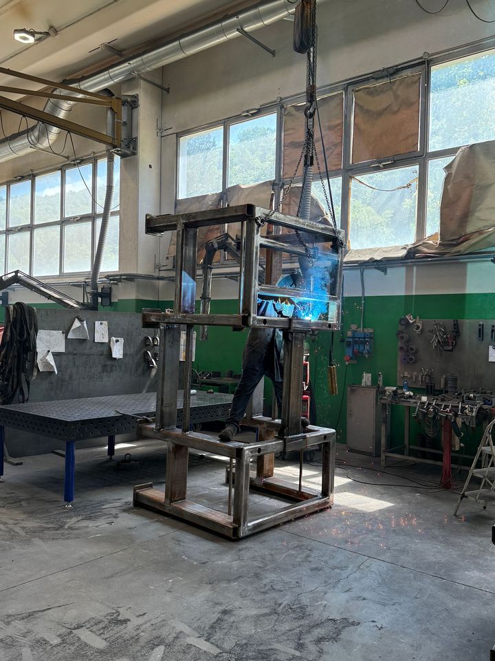 Officina industriale con struttura metallica e scintille di saldatura vicino a grandi finestre.