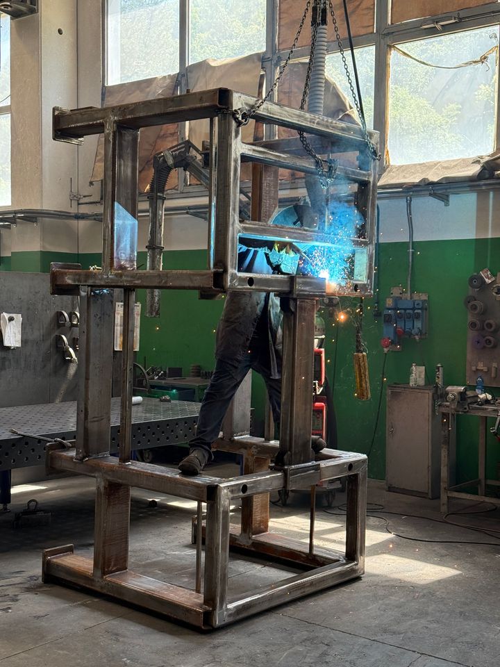 In un'officina, un impianto di saldatura industriale con scintille blu, incorniciato da impalcature metalliche e utensili.