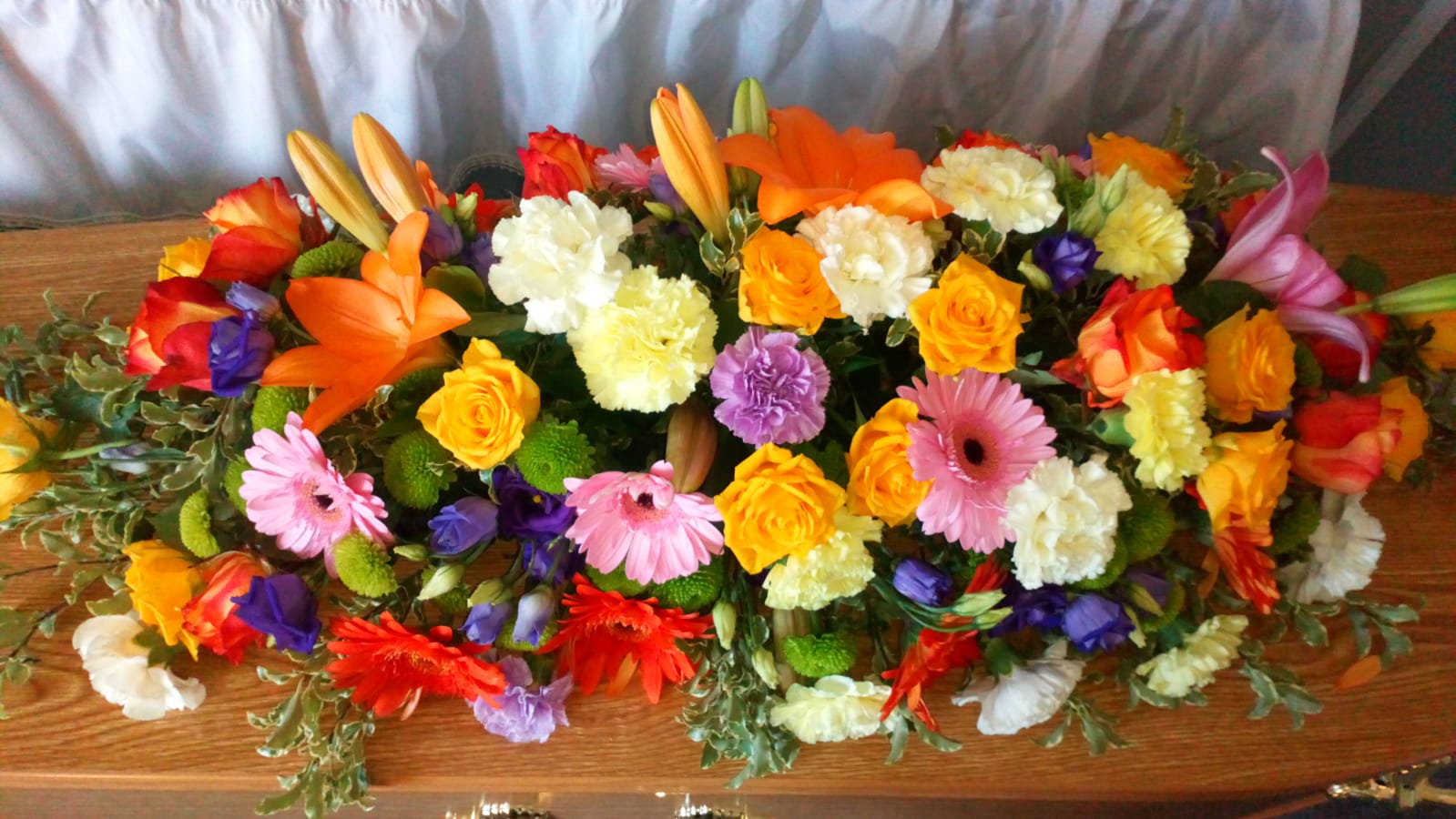 A wooden coffin covered in colorful flowers is sitting on a table.