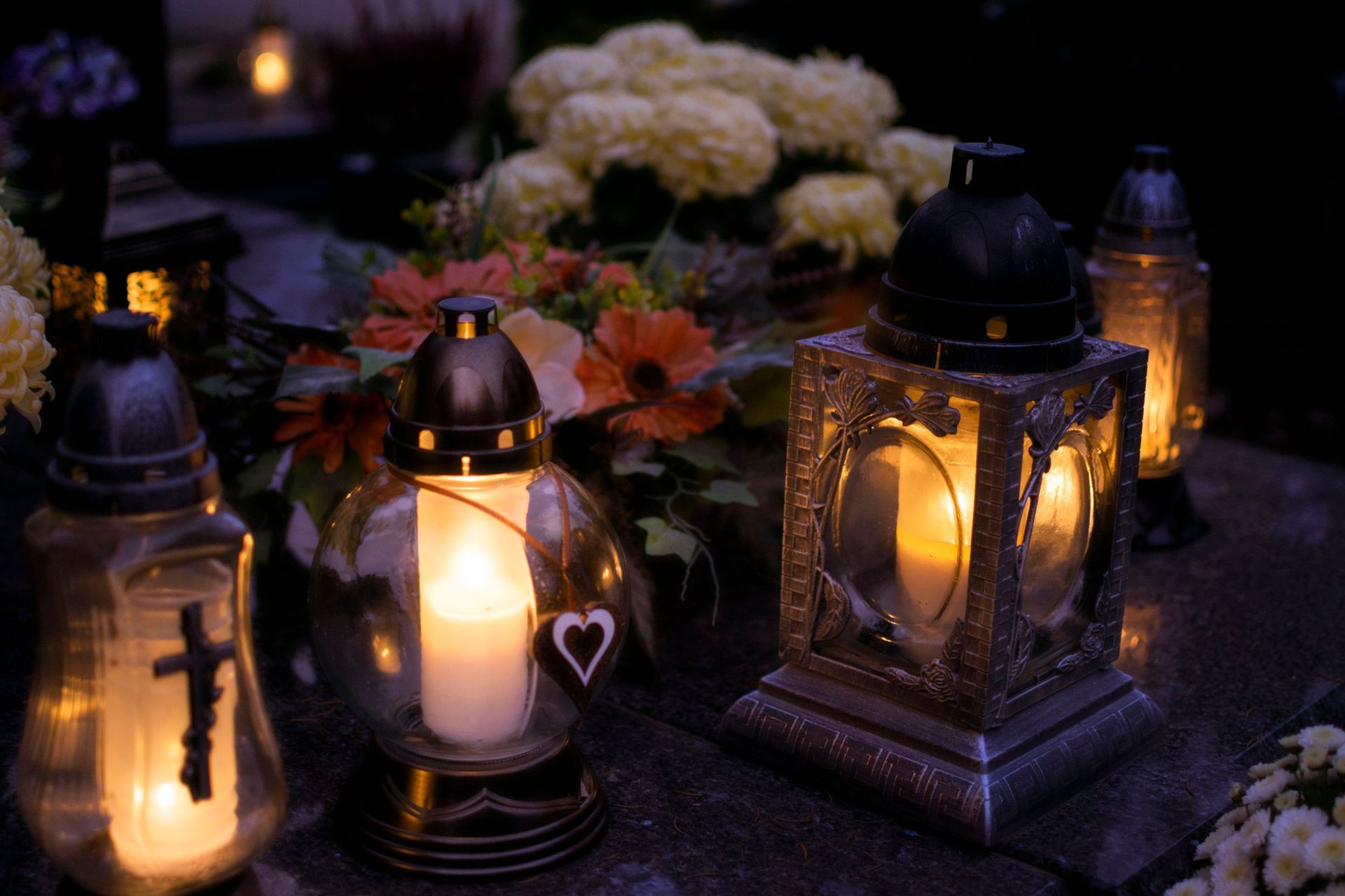 Lit lanterns and candles glowing on a dark stone surface with autumn flowers in the background