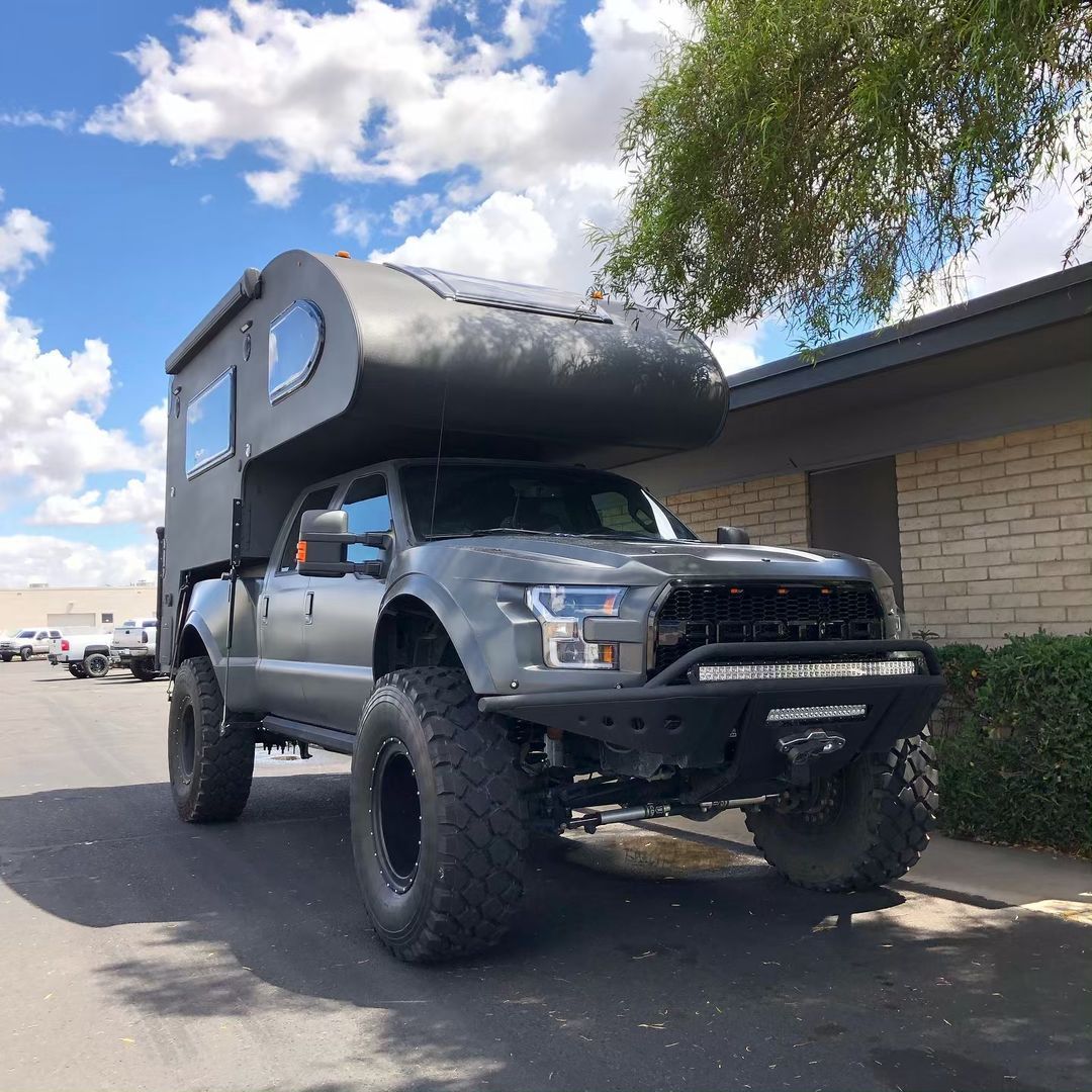 A truck with a camper on top of it is parked in front of a brick building.
