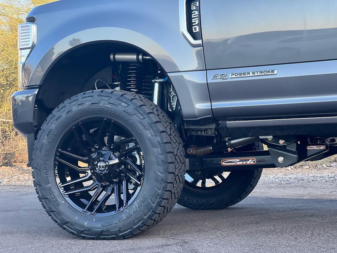 A black truck with black wheels and tires is parked on the side of the road.