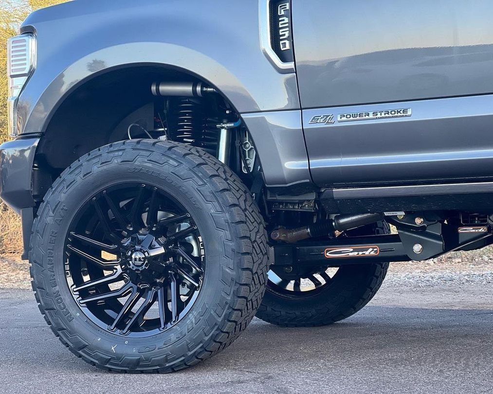 A gray truck with black wheels and tires is parked on the side of the road.