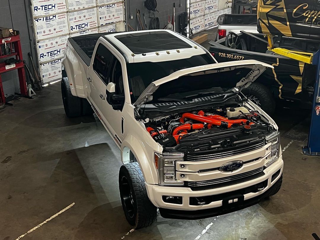 A white truck with its hood open is parked in a garage.