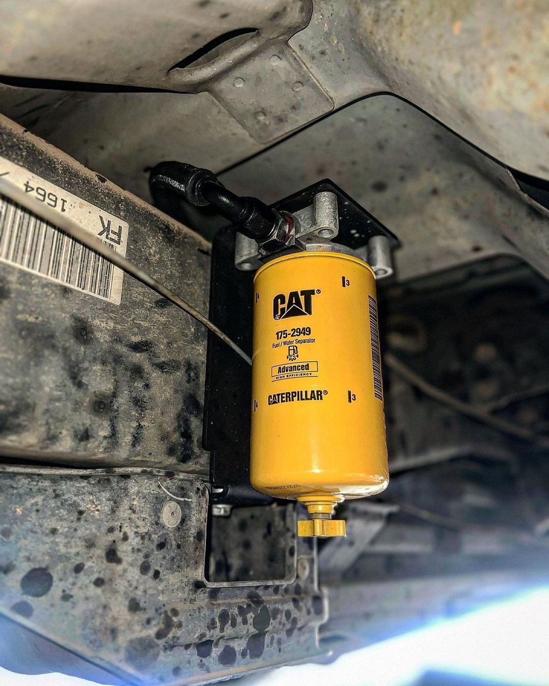 A yellow cat fuel filter is attached to the underside of a vehicle.