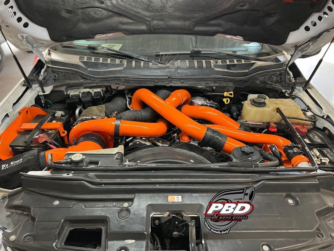 The hood of a white truck with orange hoses coming out of it.