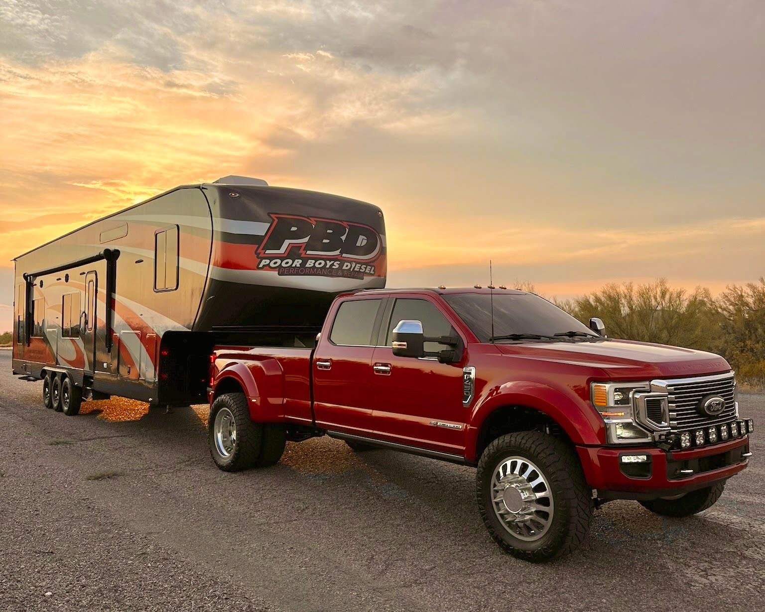 A red truck is towing a trailer on a road.