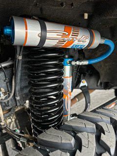 Suspension system with a black coil spring and an orange and blue shock absorber on a vehicle tire.