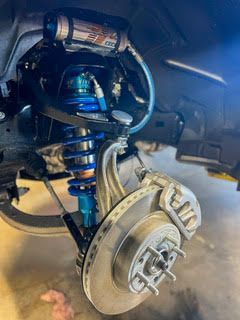 Blue and silver suspension system on a vehicle, showing shock absorber, coil spring, and brake disc.