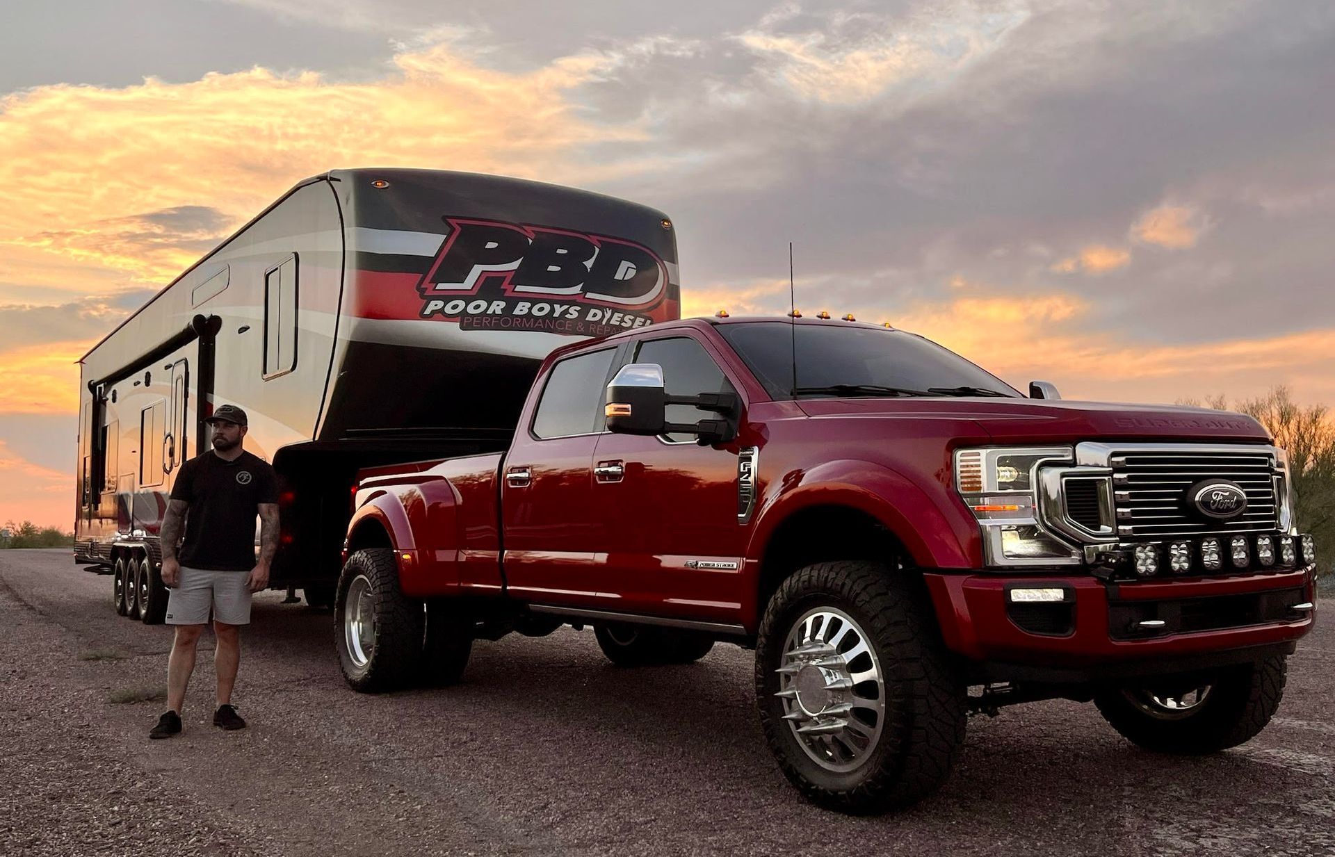 A man is standing next to a red truck with a trailer attached to it.