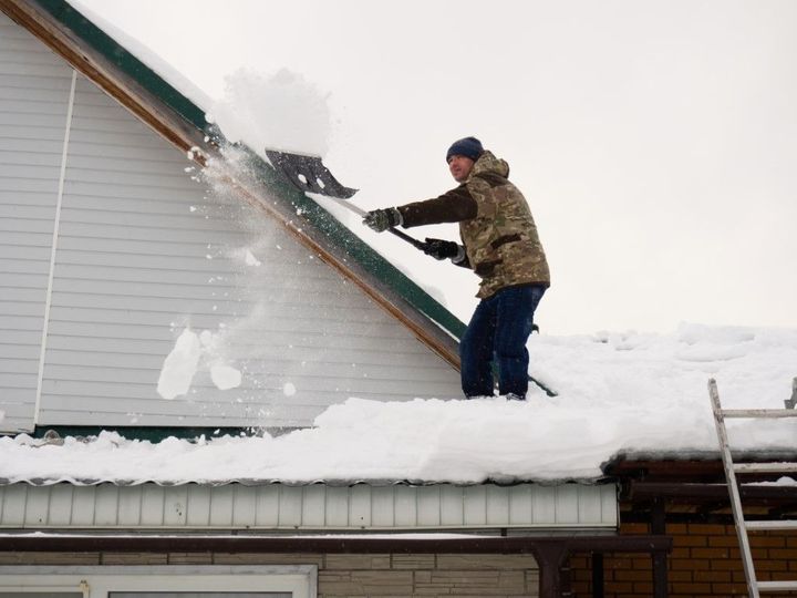 Person shoveling snow off a steep roof in winter