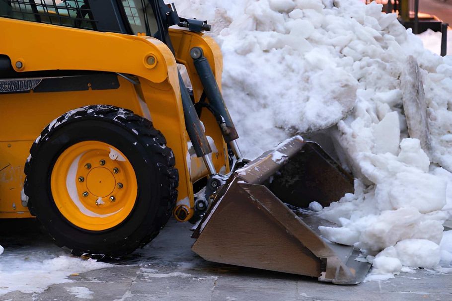 Yellow front loader pushing snow with its bucket on a snowy street