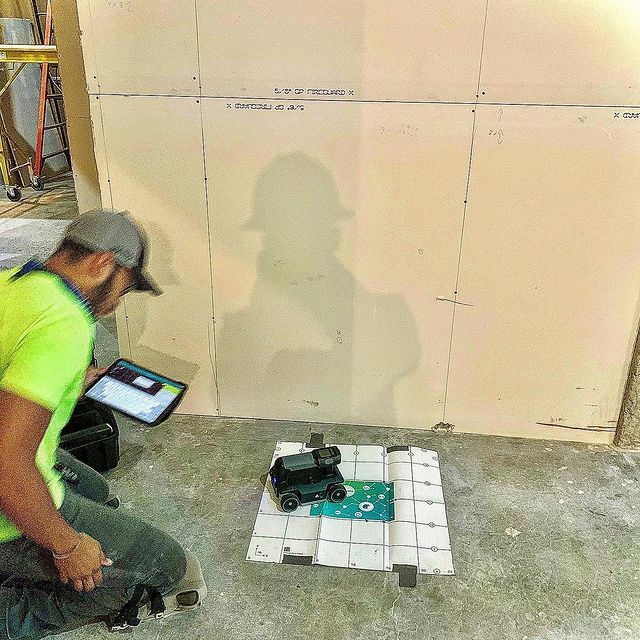 A man is kneeling on the floor looking at a tablet.