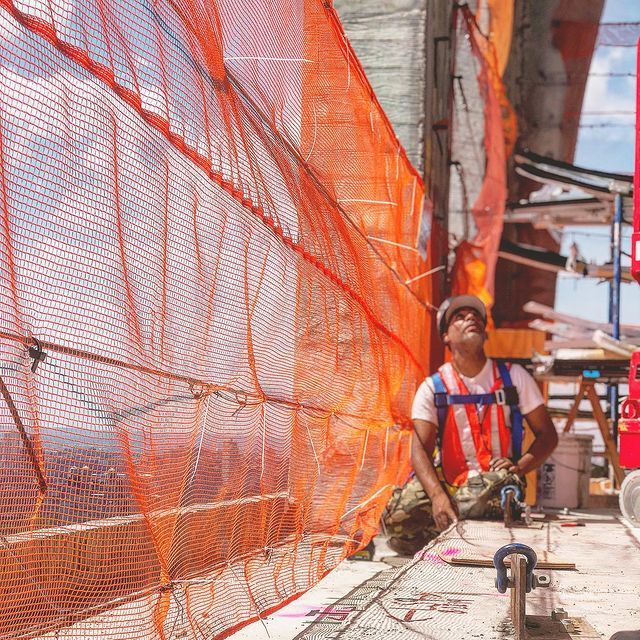 A construction worker is sitting in front of an orange net.