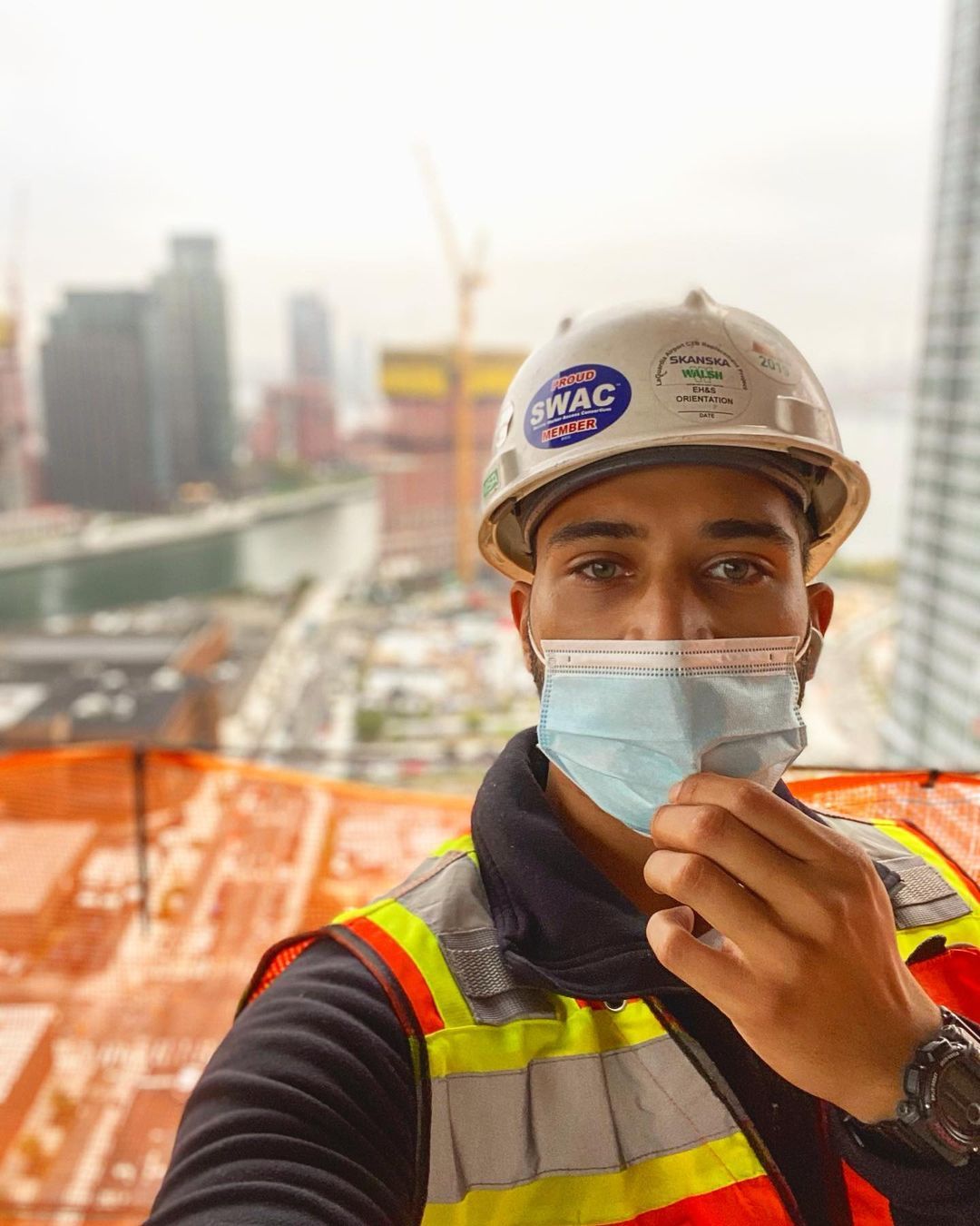 A man wearing a hard hat and a mask is taking a selfie.