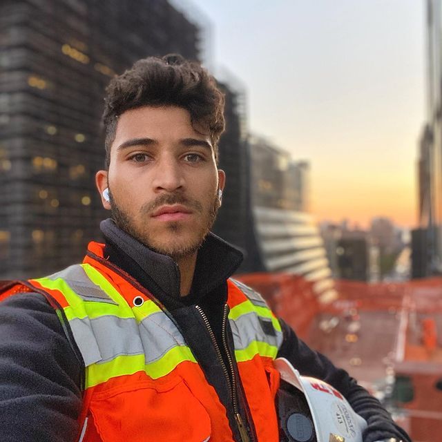 A man wearing a safety vest and a helmet takes a selfie