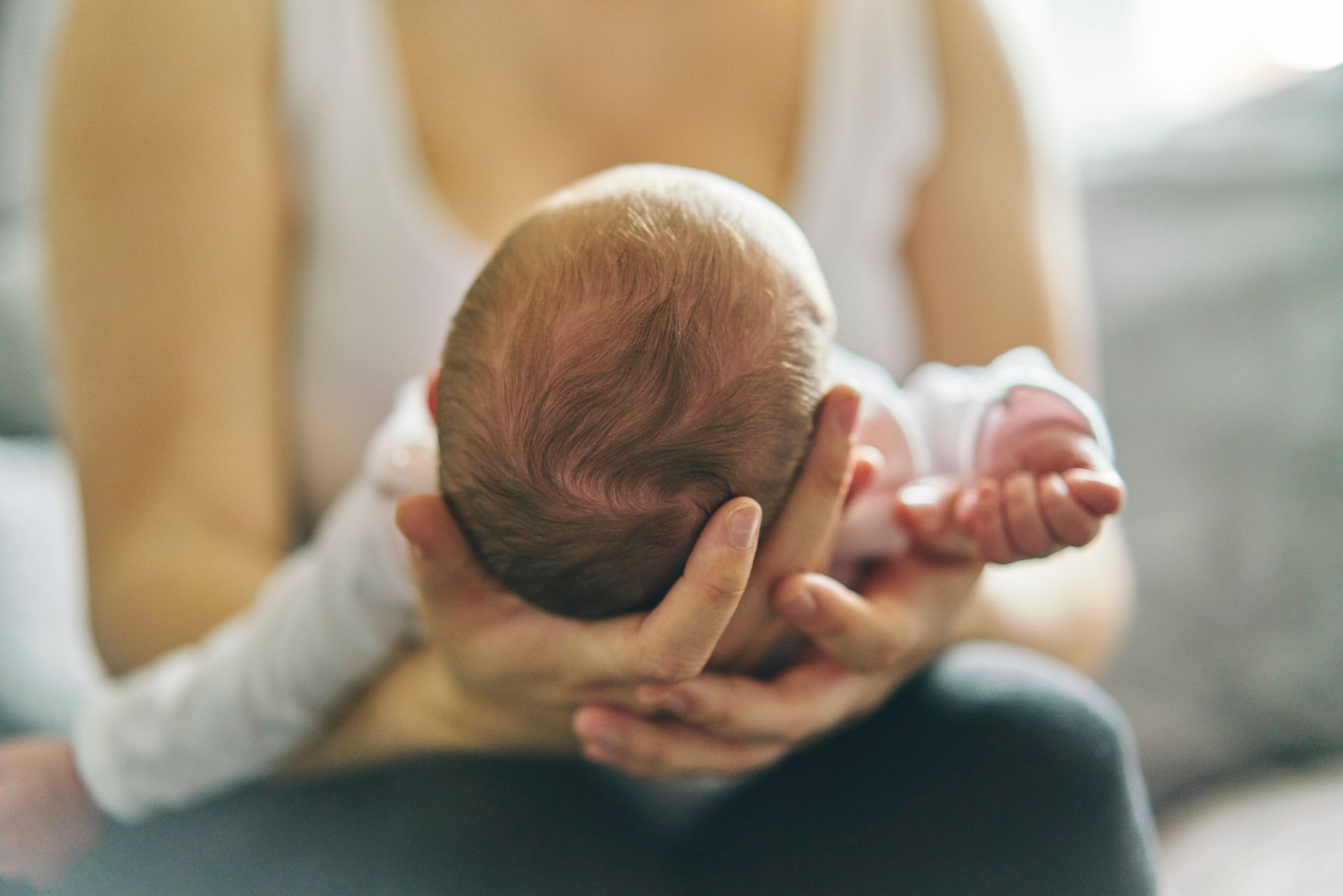 A person holding a baby, seen from the back. The baby is resting on the person’s hands.
