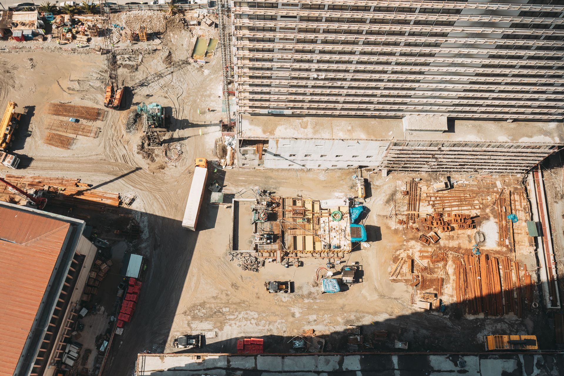 Aerial view of a construction site. Partially built structure next to dirt lot with construction materials and machinery.