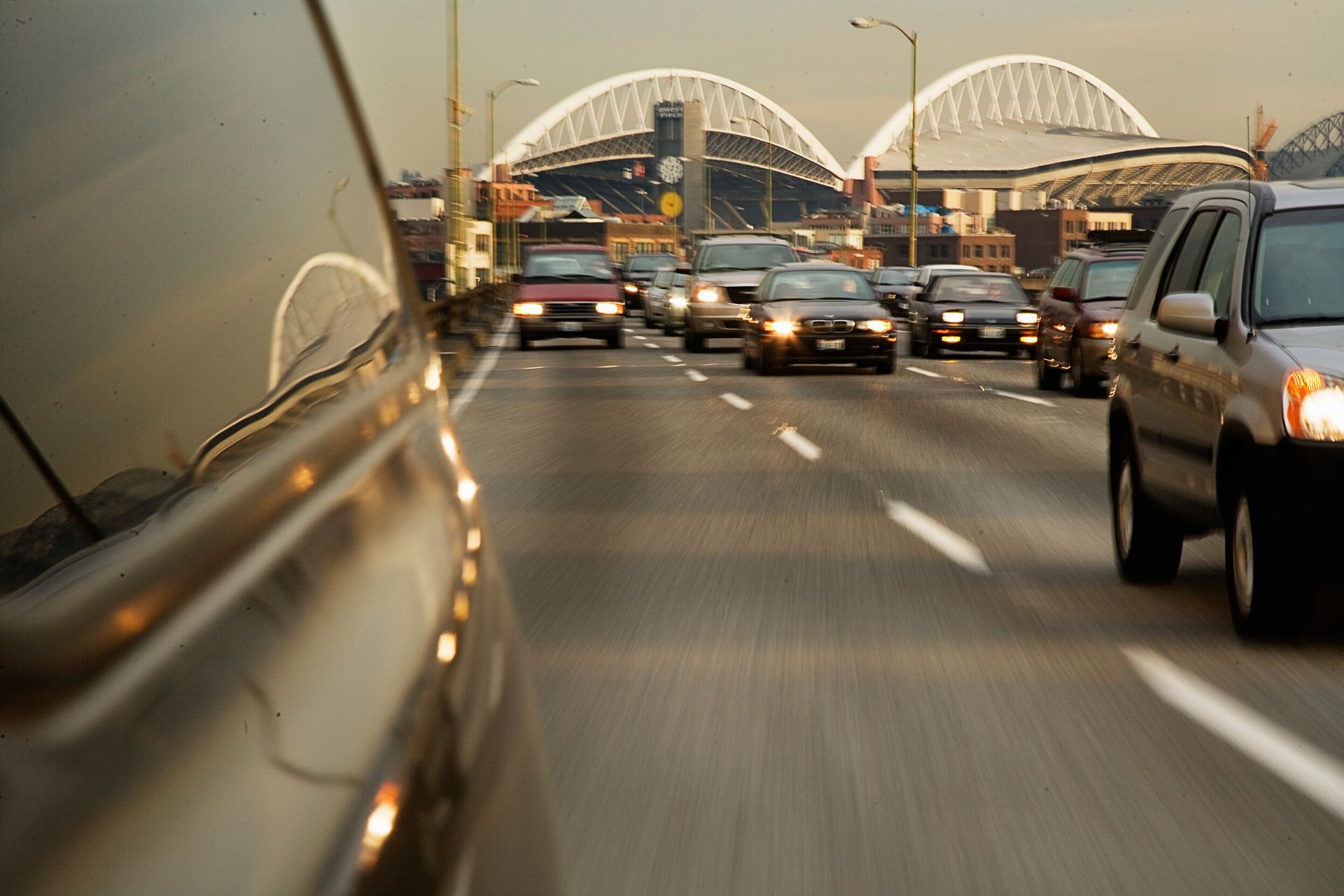 Cars in traffic on a highway, with the backdrop of an arched bridge and the sky.