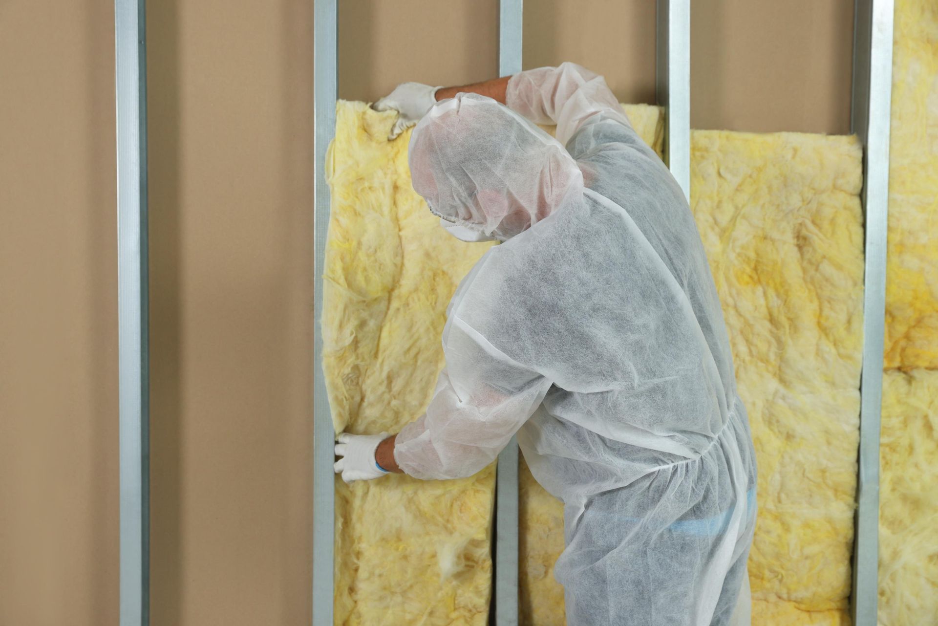 A man in a protective suit is installing insulation on a wall.