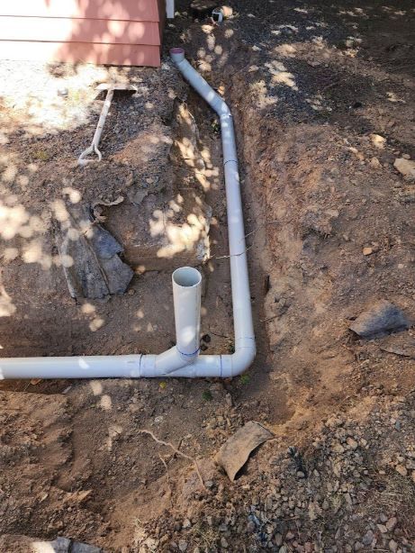 A White Pipe Is Laying In The Dirt Next To A House — RAW Plumbing & Gasfitting In Pearce, ACT